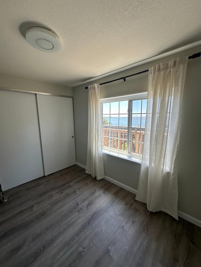 unfurnished bedroom with a closet, a textured ceiling, dark wood-style flooring, and baseboards