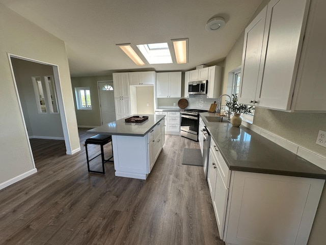 kitchen featuring white cabinets, dark countertops, appliances with stainless steel finishes, a center island, and a sink