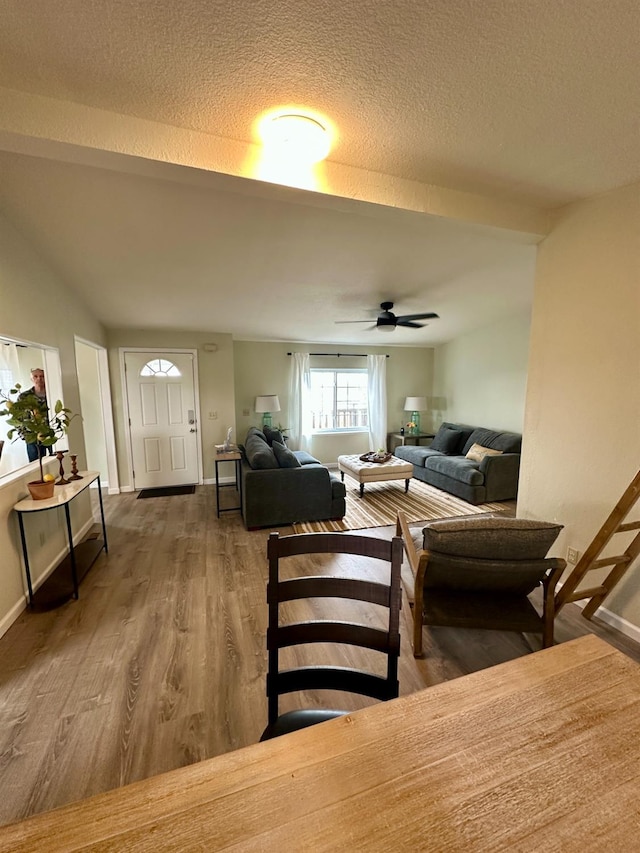 living room featuring a textured ceiling, baseboards, a ceiling fan, and wood finished floors