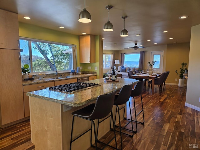 kitchen with dark wood-type flooring, decorative light fixtures, a kitchen island, and light brown cabinets