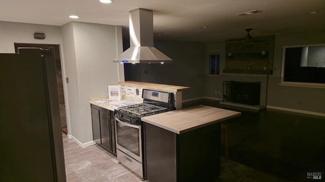 kitchen featuring visible vents, a fireplace with raised hearth, appliances with stainless steel finishes, light countertops, and exhaust hood