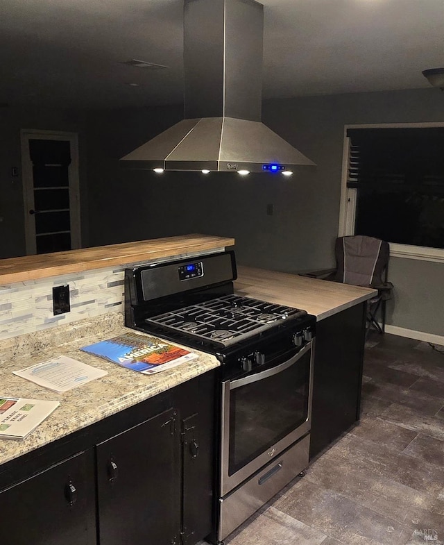 kitchen with baseboards, stainless steel gas range, island exhaust hood, light countertops, and dark cabinetry