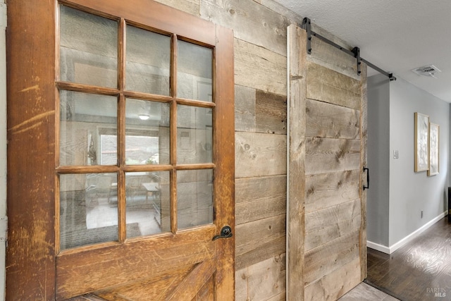 room details featuring visible vents, a barn door, a textured ceiling, wood finished floors, and baseboards