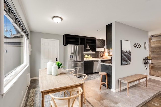 kitchen featuring stainless steel appliances, baseboards, dark cabinetry, light wood finished floors, and tasteful backsplash