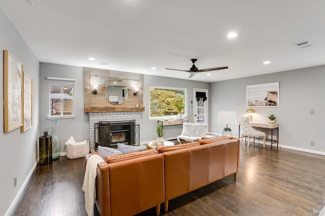 living room featuring a brick fireplace, dark wood-style flooring, visible vents, and baseboards