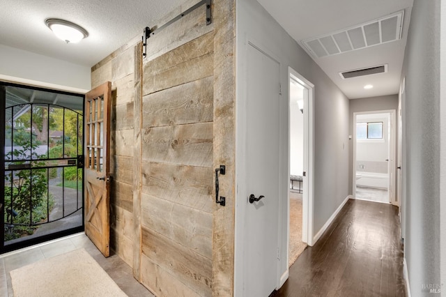 hall with a barn door, a textured ceiling, visible vents, and baseboards