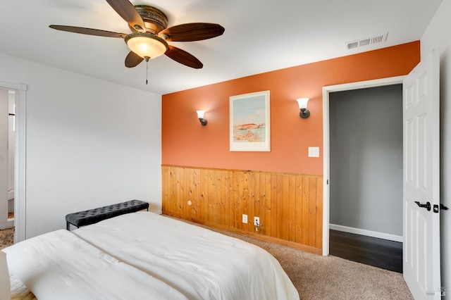 bedroom with visible vents, a ceiling fan, wainscoting, carpet floors, and wood walls