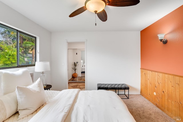 bedroom with a ceiling fan, a wainscoted wall, light colored carpet, and wooden walls