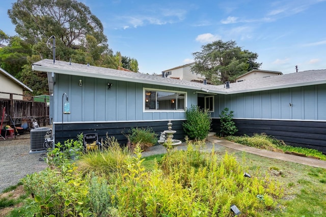 ranch-style house with board and batten siding, cooling unit, and fence