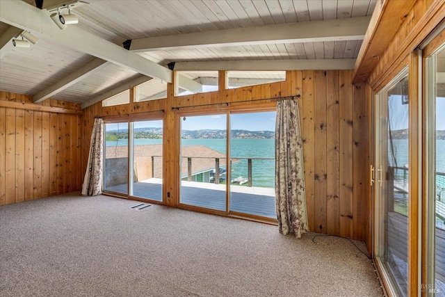 carpeted spare room with visible vents, a water view, wood walls, and lofted ceiling with beams