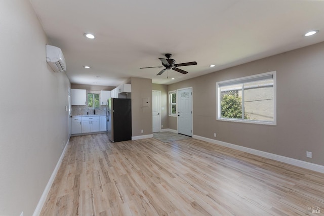 unfurnished living room featuring an AC wall unit, ceiling fan, and light wood-type flooring