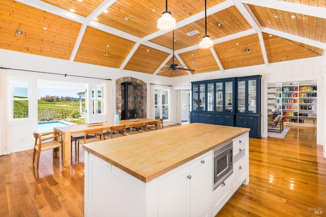 kitchen with beam ceiling, decorative light fixtures, wooden counters, wood ceiling, and a wood stove