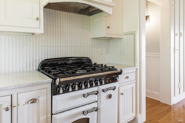 kitchen with white cabinetry, light stone countertops, light wood-type flooring, white gas range, and custom exhaust hood