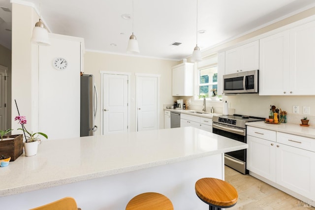 kitchen with appliances with stainless steel finishes, white cabinets, a breakfast bar, and pendant lighting