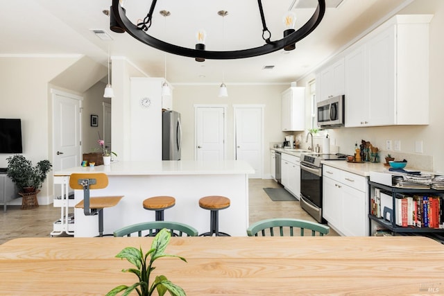 kitchen featuring stainless steel appliances, white cabinets, pendant lighting, and ornamental molding