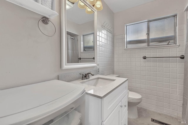 bathroom featuring vanity, tile walls, and toilet