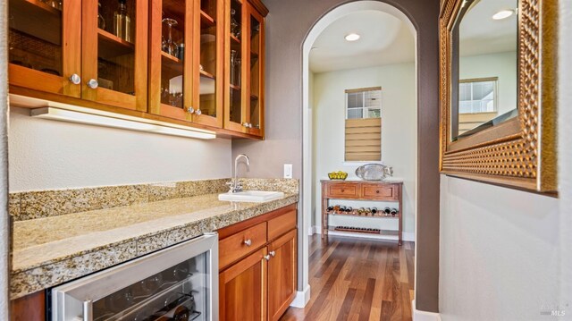 bar with sink, dark hardwood / wood-style flooring, beverage cooler, and light stone countertops