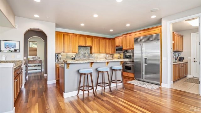 kitchen featuring stainless steel appliances, light stone counters, tasteful backsplash, a kitchen island, and a breakfast bar