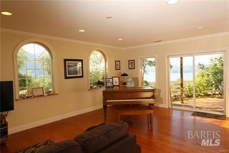 living area featuring baseboards, a healthy amount of sunlight, wood finished floors, and ornamental molding