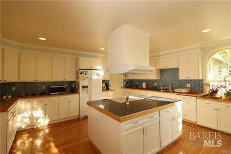 kitchen featuring white refrigerator with ice dispenser, a center island, and white cabinetry