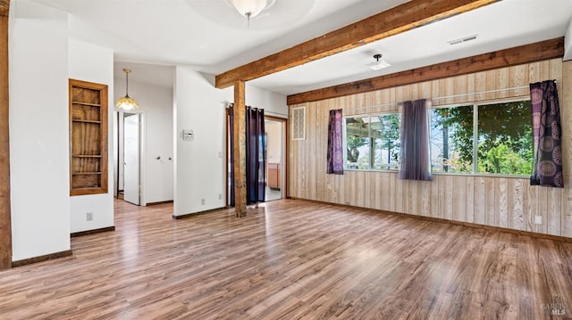 empty room featuring baseboards, visible vents, wood finished floors, wood walls, and beam ceiling