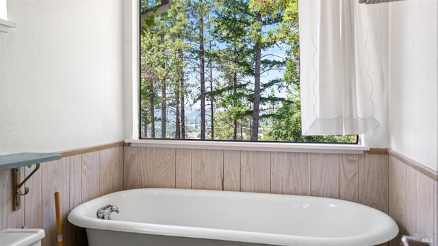 full bathroom with a soaking tub and a wainscoted wall