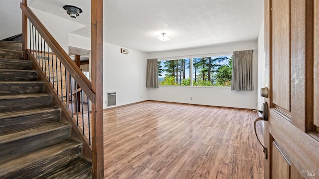 interior space with heating unit, stairway, a textured ceiling, wood finished floors, and baseboards