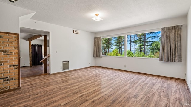 spare room with heating unit, a textured ceiling, baseboards, and wood finished floors