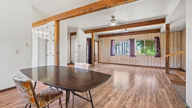 unfurnished dining area featuring wood walls, beamed ceiling, wood finished floors, and baseboards