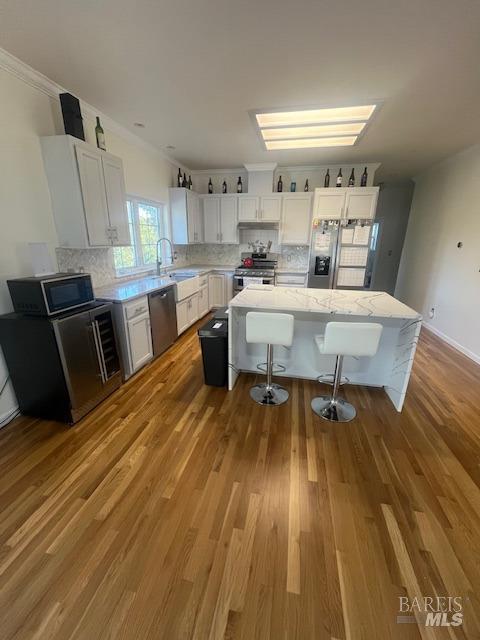 kitchen with a sink, wood finished floors, ornamental molding, appliances with stainless steel finishes, and decorative backsplash