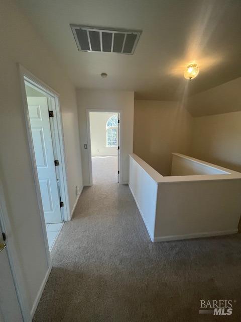 hallway with carpet, visible vents, baseboards, and an upstairs landing