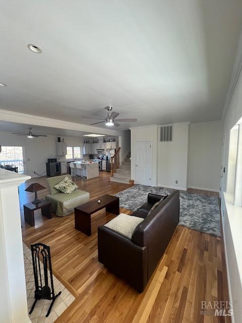 living area featuring visible vents, stairway, ceiling fan, light wood-type flooring, and baseboards