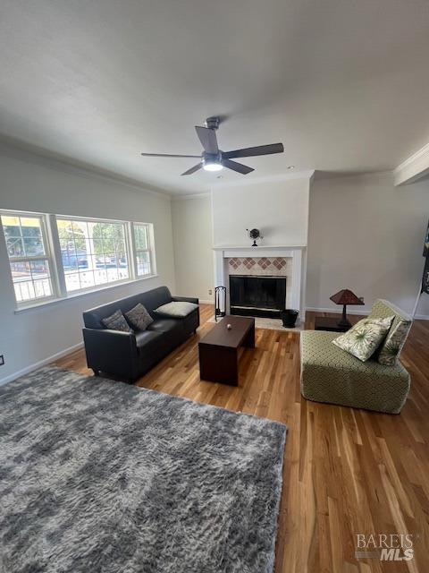 living room featuring crown molding, a ceiling fan, wood finished floors, a tile fireplace, and baseboards