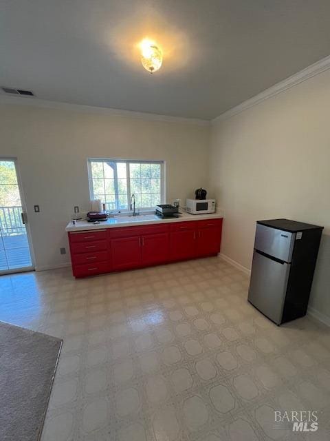 kitchen featuring visible vents, white microwave, ornamental molding, freestanding refrigerator, and a sink