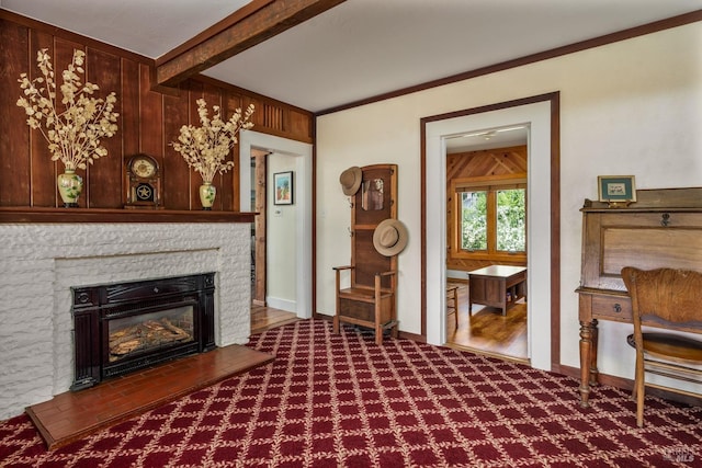 living room with a stone fireplace, wooden walls, carpet flooring, ornamental molding, and beamed ceiling