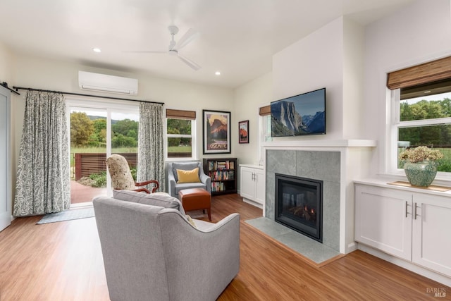 living room with light hardwood / wood-style flooring, a wall unit AC, ceiling fan, and a tiled fireplace