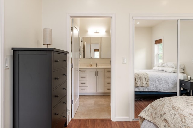 bedroom with light wood-type flooring, ensuite bathroom, a closet, and sink