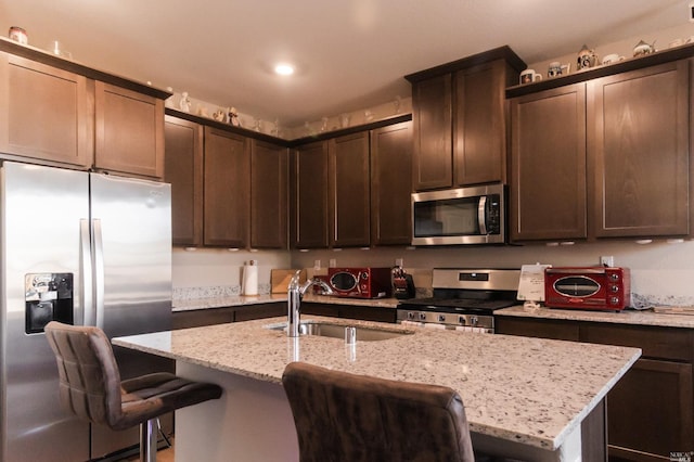 kitchen featuring light stone countertops, stainless steel appliances, a breakfast bar, and sink