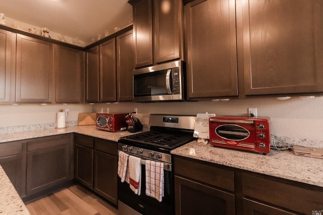 kitchen with appliances with stainless steel finishes, light stone countertops, dark brown cabinets, and light hardwood / wood-style flooring