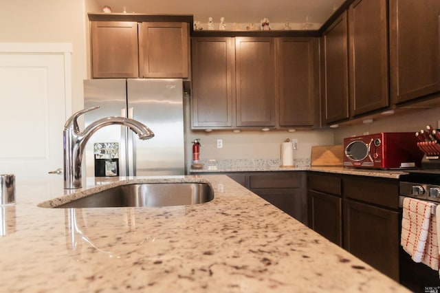 kitchen featuring dark brown cabinetry, sink, light stone counters, and stainless steel fridge with ice dispenser