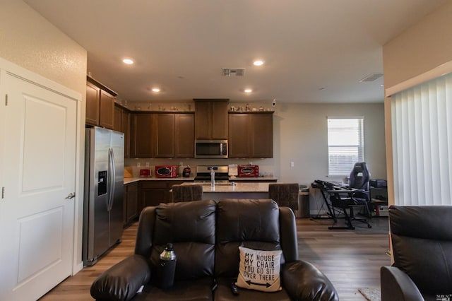 kitchen with dark brown cabinets, a center island with sink, hardwood / wood-style flooring, and appliances with stainless steel finishes