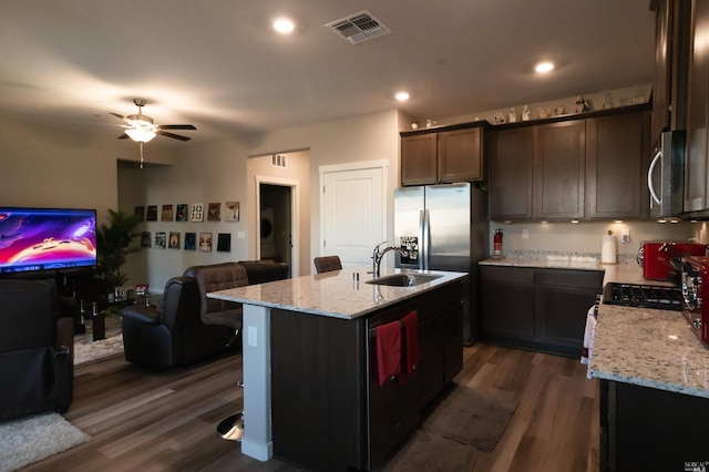 kitchen with dark wood-type flooring, an island with sink, dark brown cabinetry, sink, and ceiling fan