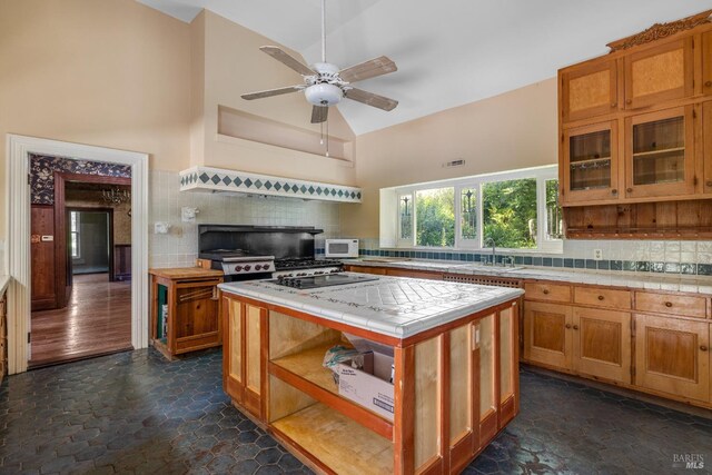 kitchen featuring sink, tasteful backsplash, high vaulted ceiling, tile counters, and a kitchen island