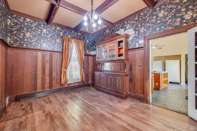 empty room with an inviting chandelier, coffered ceiling, a baseboard radiator, beamed ceiling, and light wood-type flooring