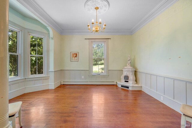 empty room with an inviting chandelier, a baseboard heating unit, a wealth of natural light, and ornamental molding