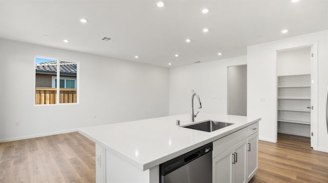 kitchen featuring sink, dishwasher, white cabinetry, light hardwood / wood-style floors, and an island with sink