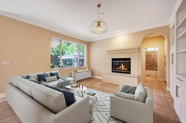 living room with light tile patterned flooring, baseboards, ornamental molding, a tiled fireplace, and arched walkways