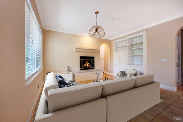 tiled living area featuring baseboards, a tiled fireplace, arched walkways, and ornamental molding