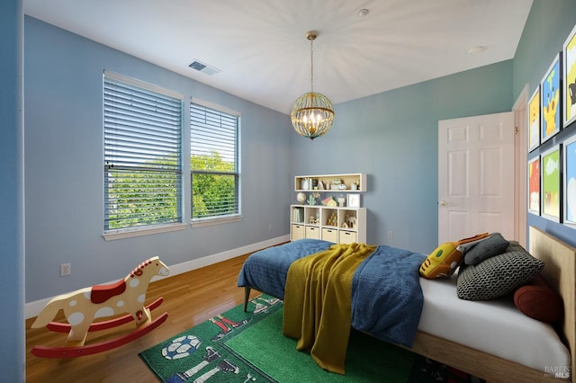bedroom with baseboards, visible vents, a notable chandelier, and wood finished floors
