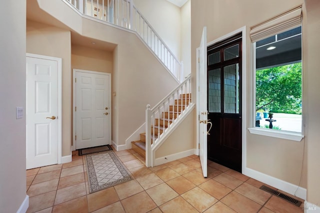 entryway with stairs, light tile patterned floors, baseboards, a high ceiling, and visible vents